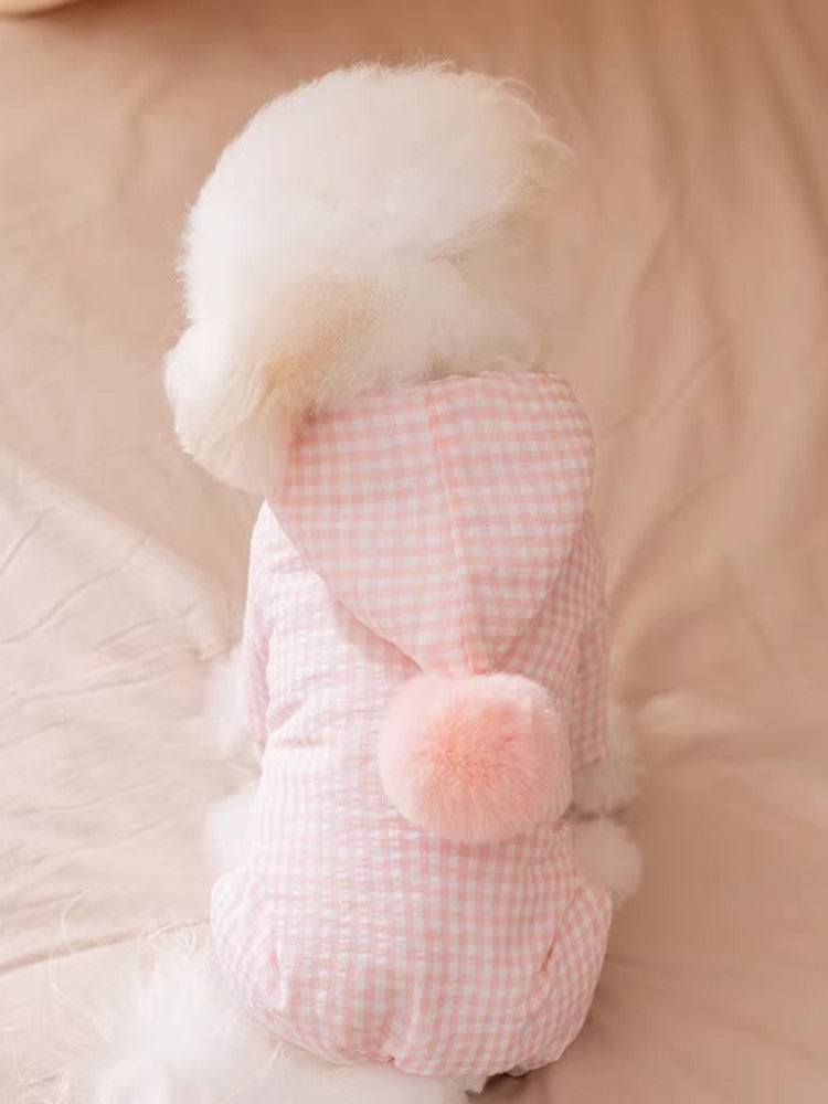 Rear view of a fluffy white dog in a pink gingham dog coat with a pink pom-pom.