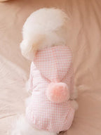 Rear view of a fluffy white dog in a pink gingham dog coat with a pink pom-pom.