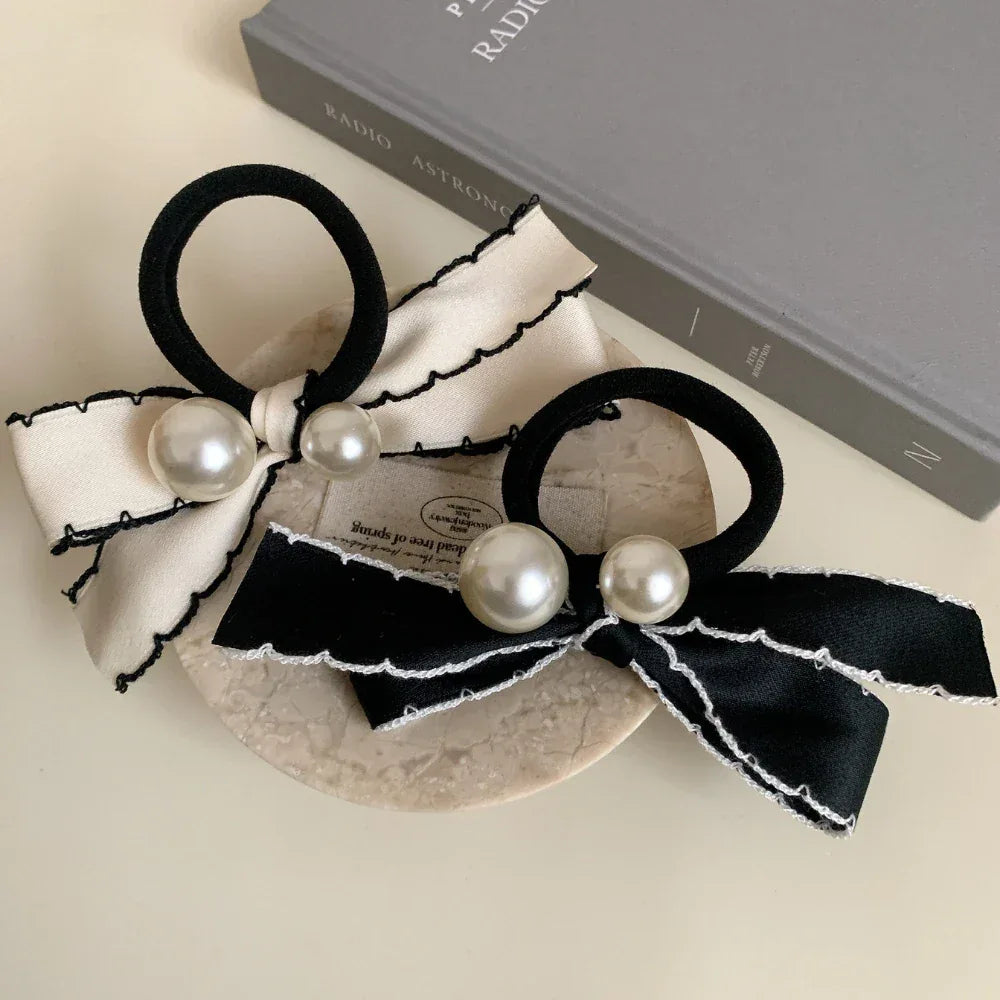 Two bow hair ties, one cream and one black, with pearl embellishments, are arranged on a surface with a book.