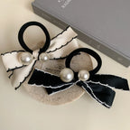 Two bow hair ties, one cream and one black, with pearl embellishments, are arranged on a surface with a book.