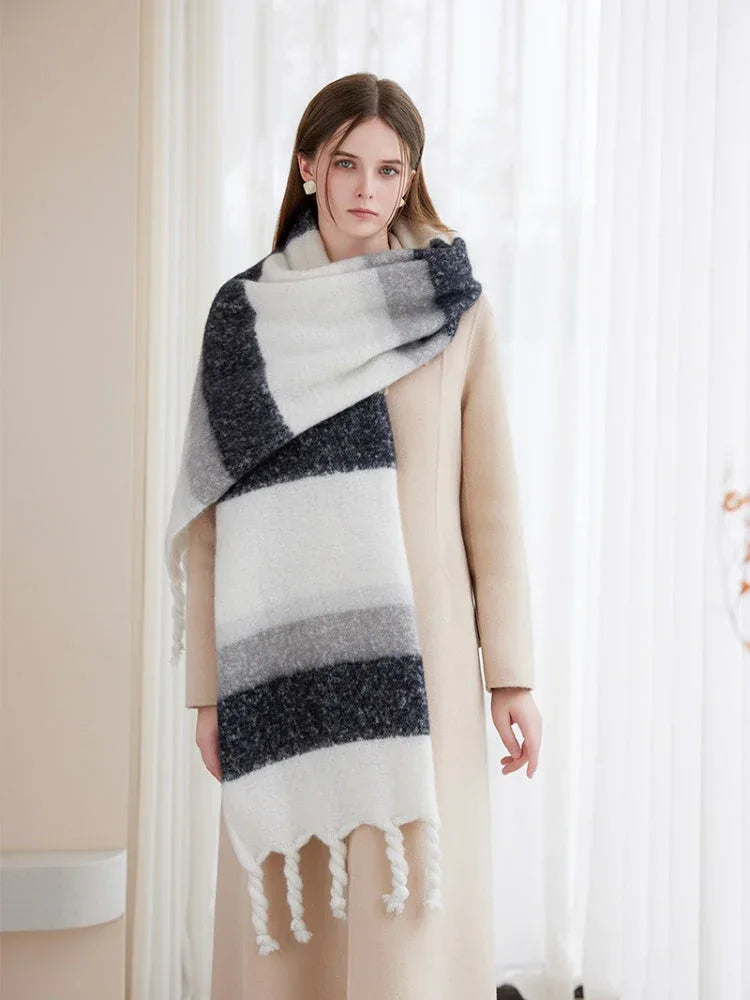 Woman modeling a cream coat and a versatile, oversized striped scarf in white, grey, and dark blue.