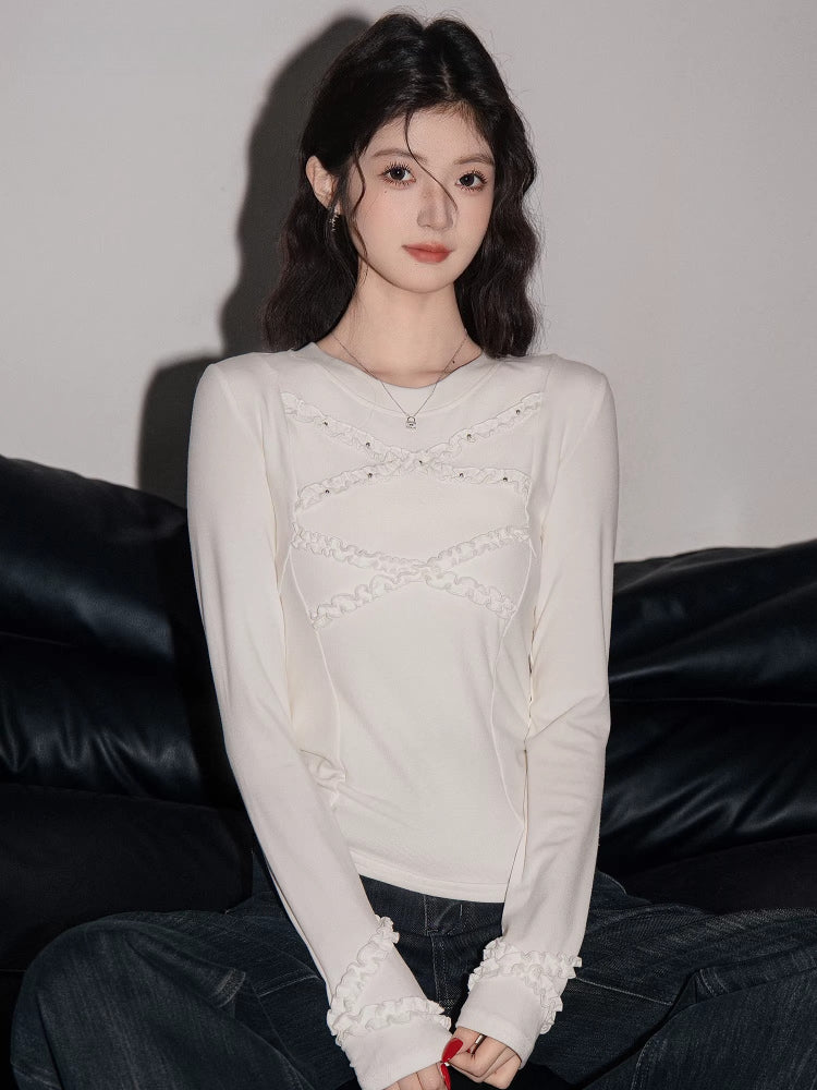 Woman sitting on a black sofa wearing a white long-sleeved top with ruffled detailing and dark wash jeans.
