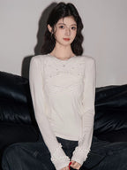 Woman sitting on a black sofa wearing a white long-sleeved top with ruffled detailing and dark wash jeans.