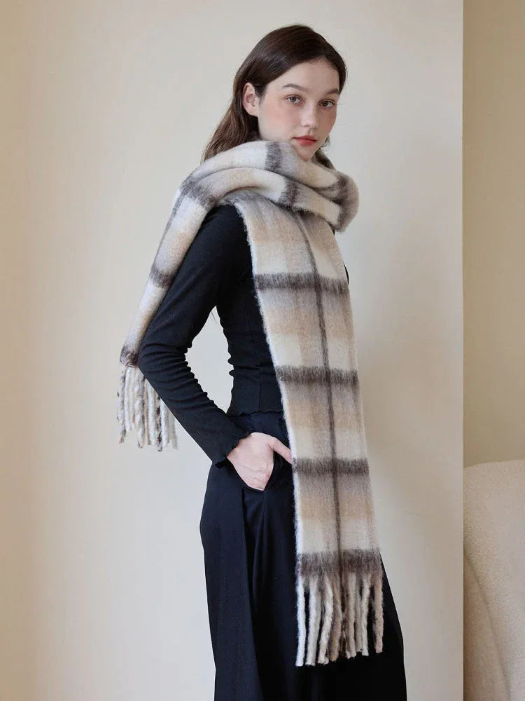 Woman wearing a black long-sleeve shirt and black wide-leg pants, accessorized with a large, soft plaid scarf in cream, beige, and brown tones with fringed ends.