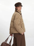Side view of a woman wearing a tan corduroy puffer jacket with a repeating dog print, brown wide-leg pants, and a brown cap.