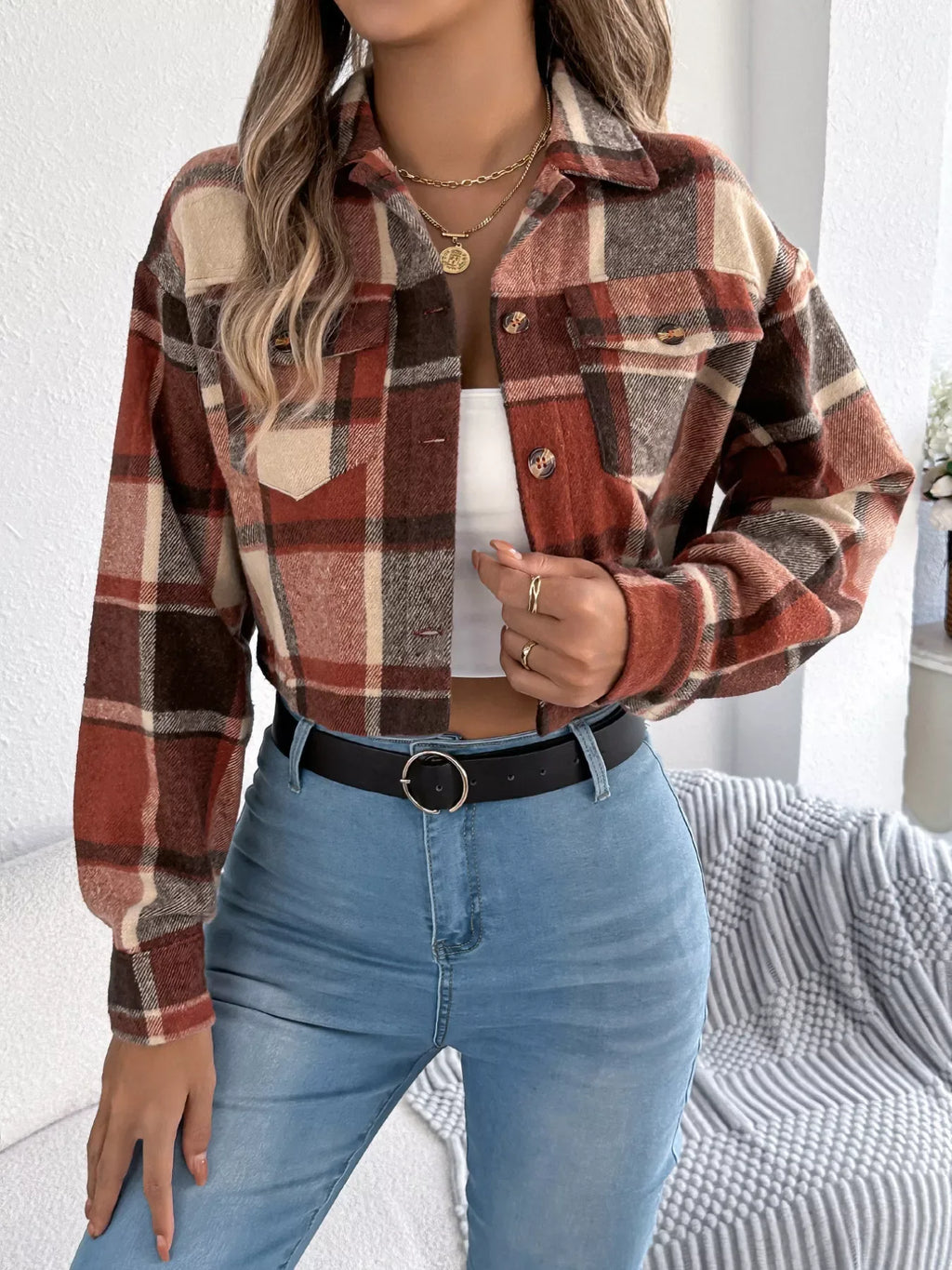 Model wearing a cropped plaid jacket over a white tank top and blue jeans.