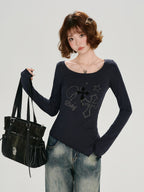 Woman wearing a dark blue long-sleeve top with a scoop neckline and flared cuffs, styled with denim jeans and a black bag.