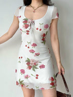 Close-up of a woman's torso in a white mesh dress with a strawberry and rose pattern, showcasing the tie-front detail.