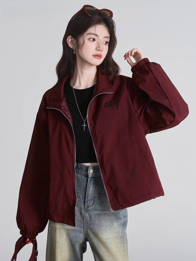Woman wearing a maroon bomber jacket, black crop top, and light wash jeans