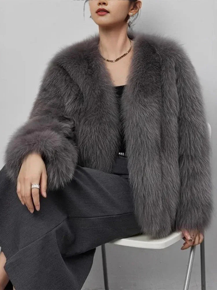 Woman sitting down wearing a grey faux fur cropped jacket.