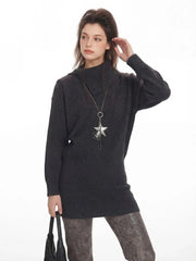 Model posing in a charcoal grey oversized turtleneck knit tunic, showcasing the texture and neckline, with a hint of the patterned leggings and leg warmers below.