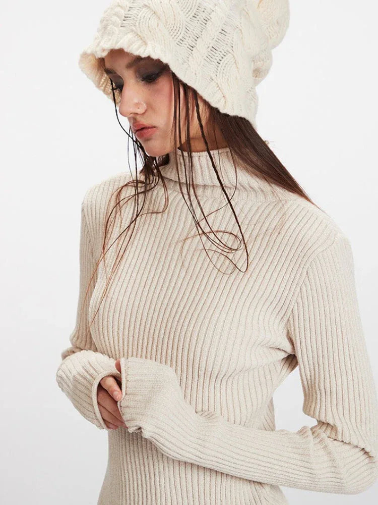 Close-up of a model wearing a cream ribbed turtleneck sweater with integrated fingerless arm warmers and a cream knit beanie.