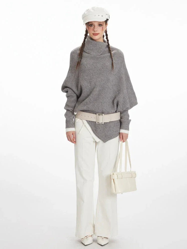 Woman wearing a grey asymmetrical knit poncho with a turtleneck, white pants, and a white belt, front view Main image