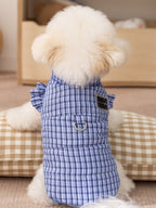 The back of a white dog wearing a blue plaid dog vest, showing the d-ring and logo detail.