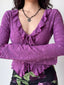 Woman wearing a purple floral lace long-sleeve top with a tie-front closure and a floral necklace.