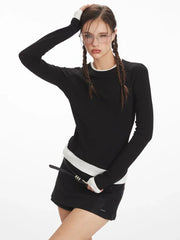 Woman winking and touching her hair, wearing a black long-sleeved top with white trim, black shorts, and glasses.