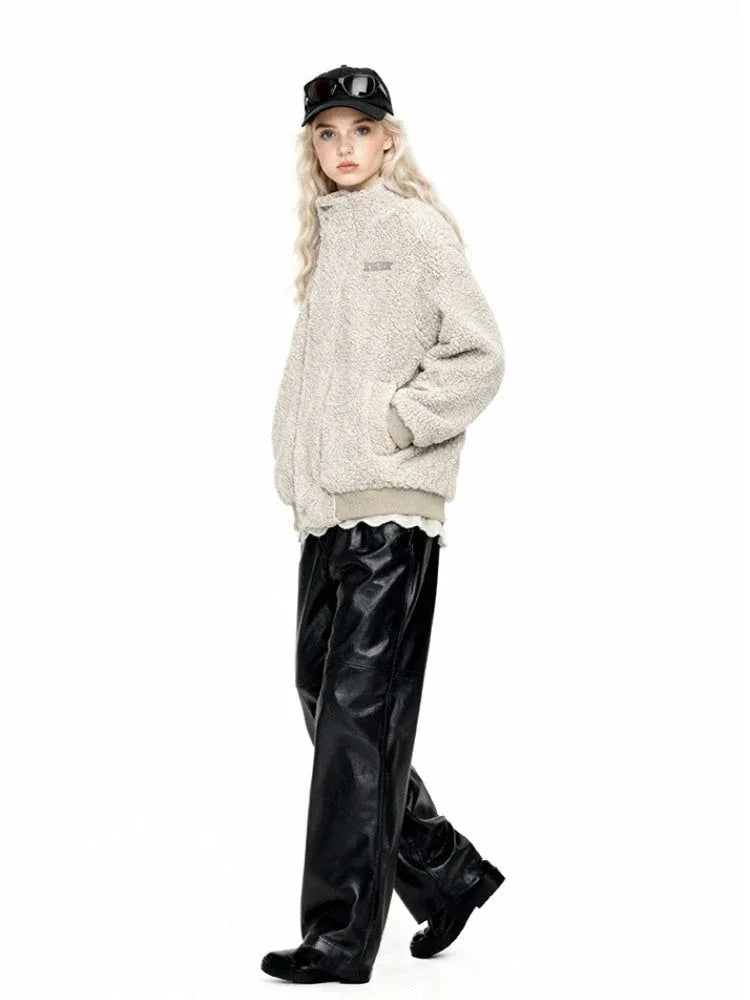 Woman in a cream-colored sherpa fleece bomber jacket and black faux leather pants walking to the side.