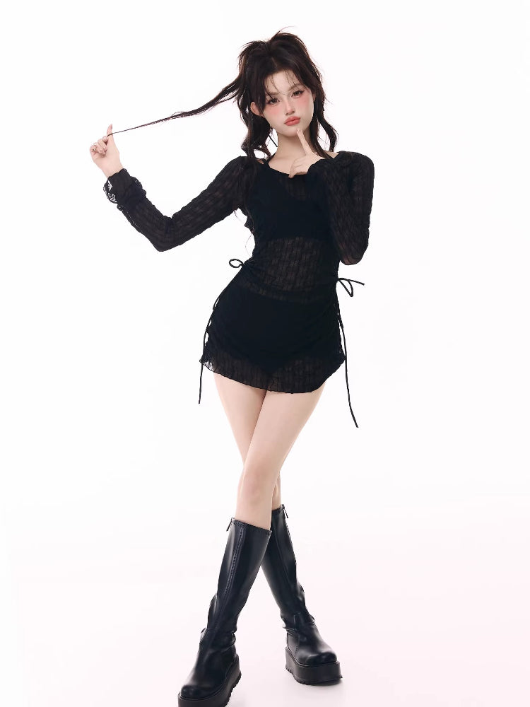 Model posing in a black sheer long-sleeve top, black shorts, and black platform boots.