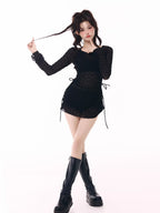 Model posing in a black sheer long-sleeve top, black shorts, and black platform boots.