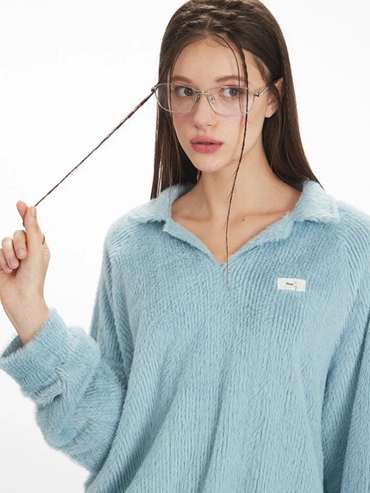 Close-up of a model wearing a light blue fuzzy knit collared v-neck sweater, showing the texture of the fabric and a small white tag on the chest.