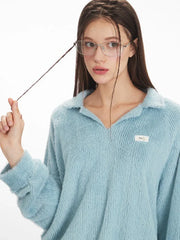 Close-up of a model wearing a light blue fuzzy knit collared v-neck sweater, showing the texture of the fabric and a small white tag on the chest.