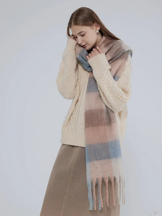 Woman wearing a cream cable knit sweater and a plaid scarf, hugging herself.