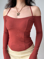 Woman in a rust-colored ribbed knit top with off-the-shoulder long sleeves and a halter neckline, showcasing the fitted silhouette.
