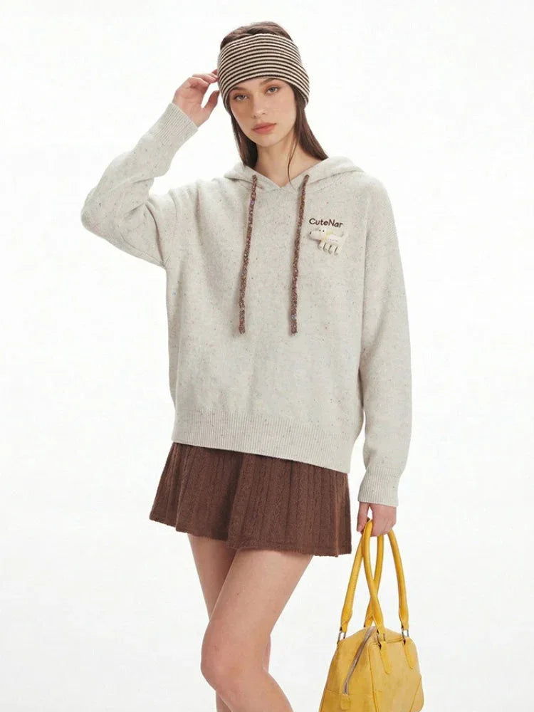 Model adjusting her striped headband while wearing a speckled knit hoodie, brown pleated skirt, and cream boots.