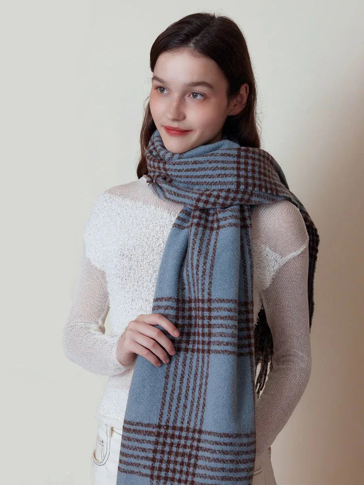 Woman holding a blue and brown plaid scarf with fringe detail