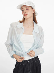 Woman wearing a light blue sheer button-down shirt untied and open over a white tube top, dark wash wide-leg jeans, and a white and blue striped headscarf.