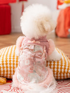 Rear view of a white Bichon Frise dog wearing a pink floral embroidered vest with faux fur trim, sitting on a cushion.