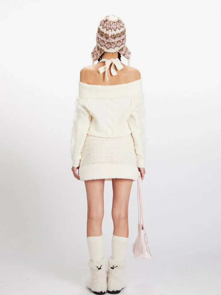 Back view of a model wearing a cream off-the-shoulder knit sweater and a matching mini skirt, with an ear flap hat and pink handbag. Secondary image
