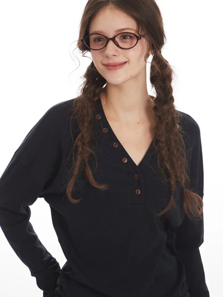 Extreme close-up of a woman's face wearing a dark long-sleeved V-neck top, showing the button details and her braided hair.