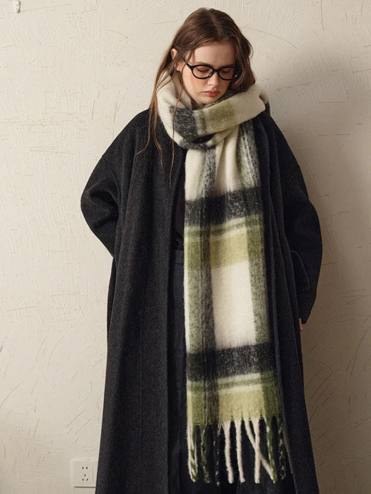 woman wearing a dark coat and a green and white plaid scarf, looking down