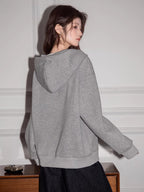 Rear view of a woman wearing a grey V-neck oversized hoodie.