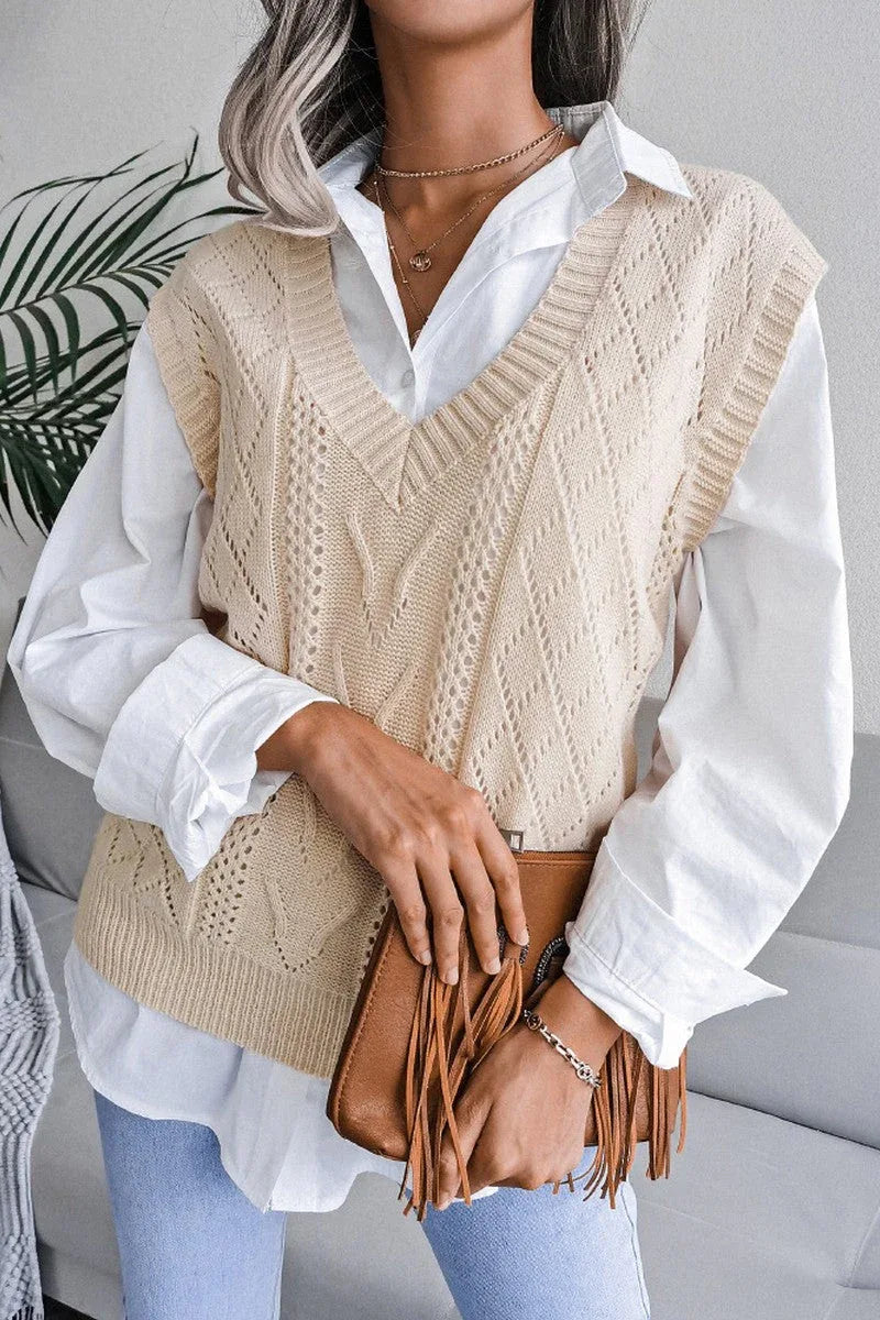 Front view of a woman wearing a cream knit V-neck sleeveless vest over a white collared shirt, holding a brown fringed clutch.