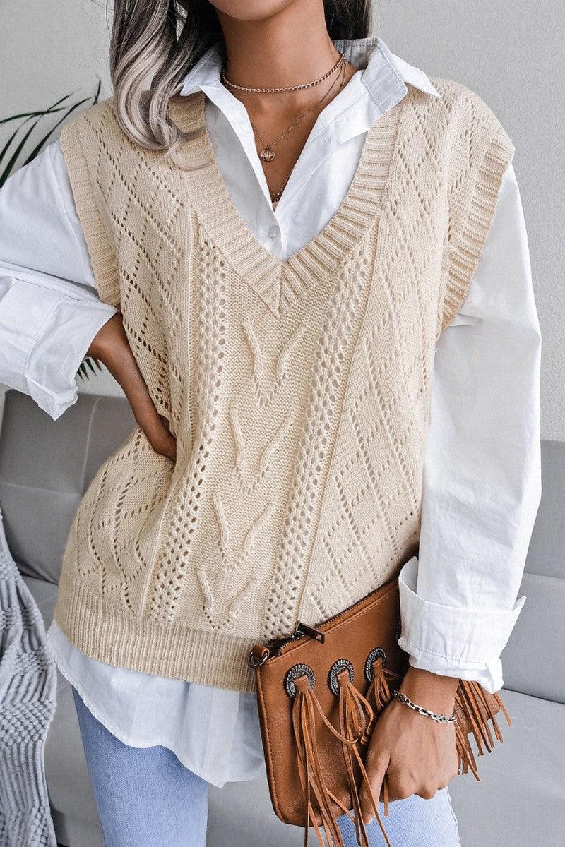 Close-up of a woman wearing a cream knit V-neck sleeveless vest over a white collared shirt, holding a brown fringed clutch.