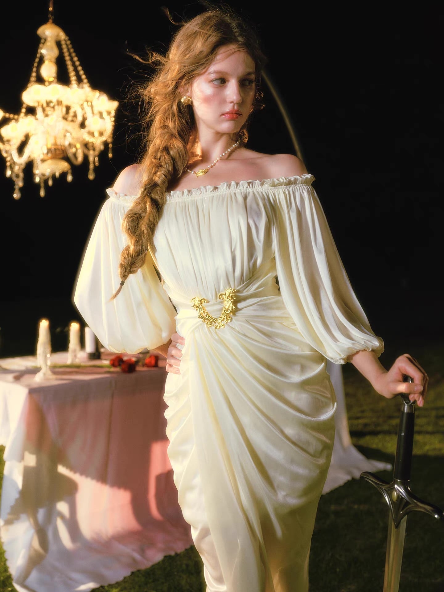 Full body shot of a woman in an elegant cream satin dress with an off-the-shoulder design, highlighting the ruched detailing and leg slit.
