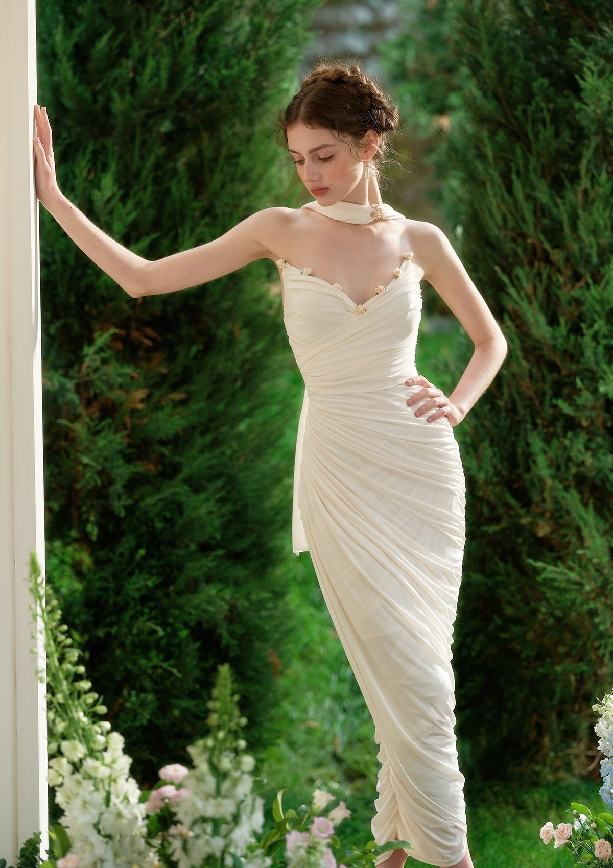 Full body shot of a model wearing a cream satin off-the-shoulder gown with intricate ruching and floral details.