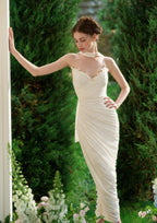 Full body shot of a model wearing a cream satin off-the-shoulder gown with intricate ruching and floral details.