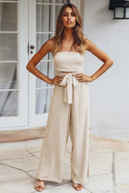 woman wearing a beige strapless jumpsuit with wide-leg pants and a tie-waist detail, front view