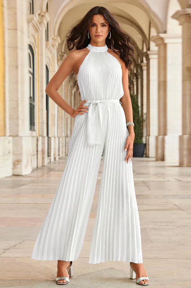 Woman standing in a white pleated halter neck wide leg jumpsuit.