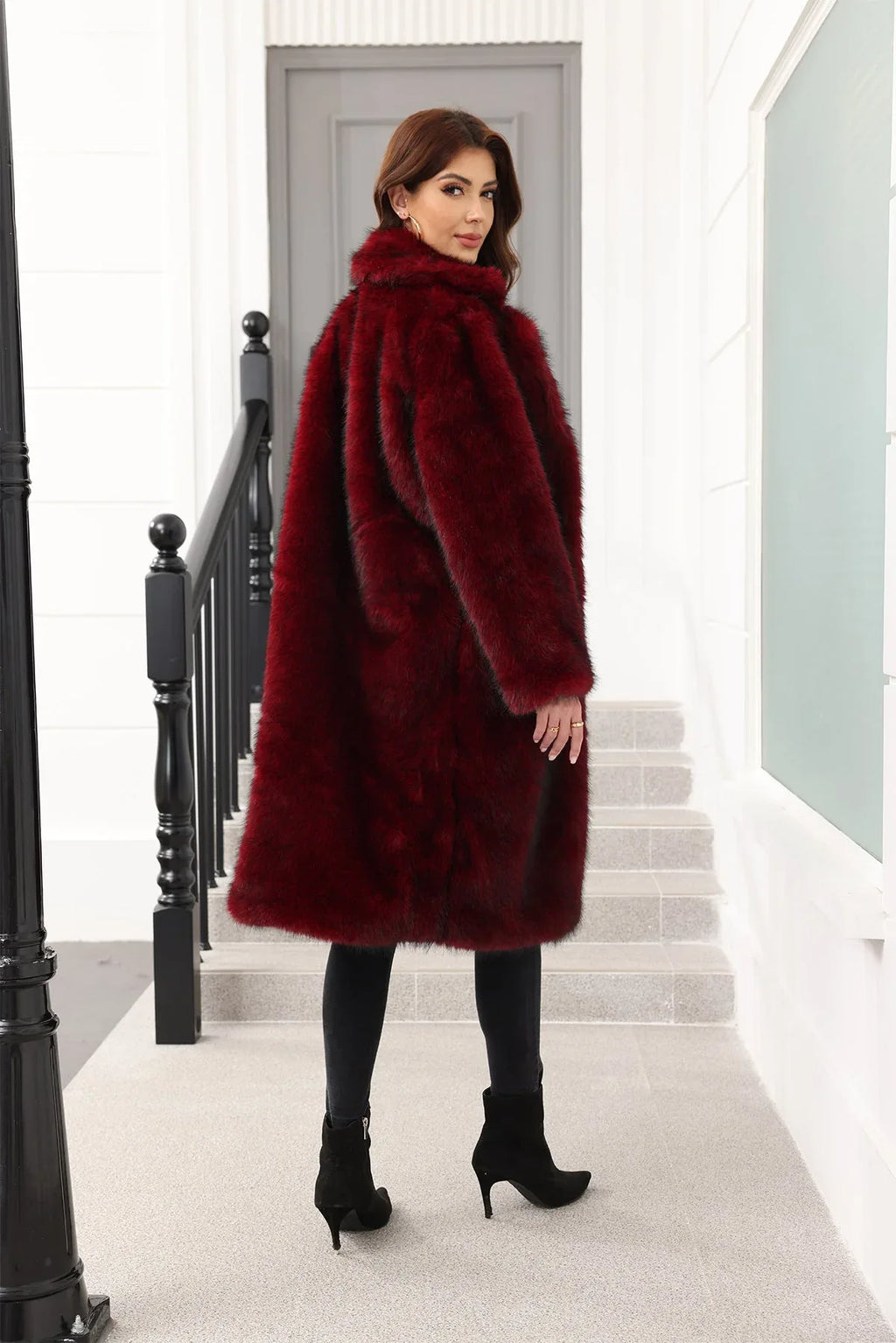 A woman wearing a long, burgundy faux fur coat over a black top and black pants, viewed from the back.