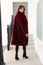 A woman wearing a long, burgundy faux fur coat over a black top and black pants, viewed from the back.
