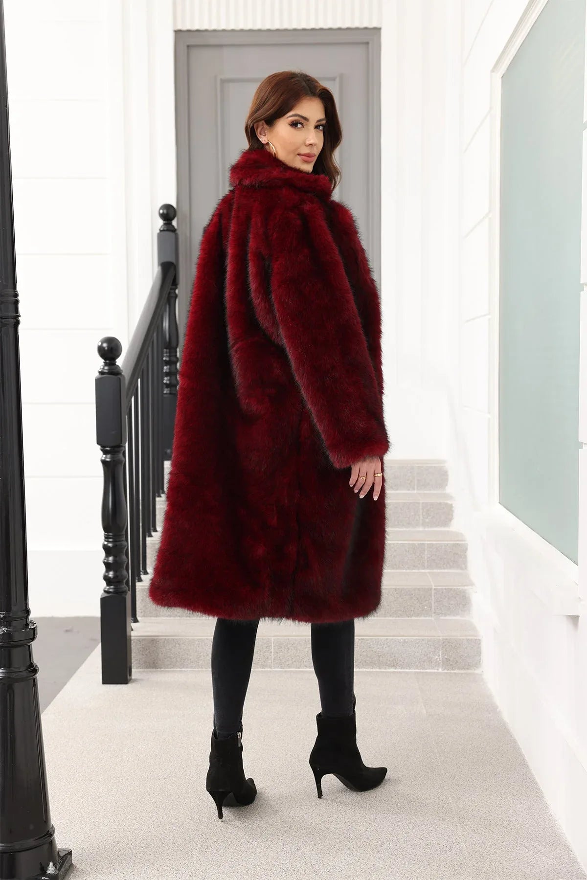 A woman wearing a long, burgundy faux fur coat over a black top and black pants, viewed from the back.