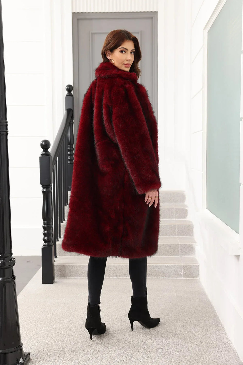 A woman wearing a long, burgundy faux fur coat over a black top and black pants, viewed from the back.