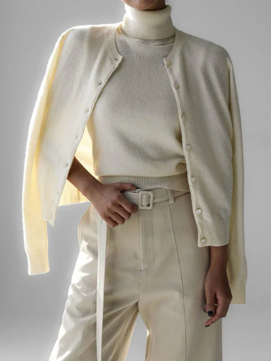 Woman wearing a cream-colored cashmere cardigan over a matching turtleneck and cream-colored trousers with a white belt. Secondary image