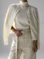 Woman wearing a cream-colored cashmere cardigan over a matching turtleneck and cream-colored trousers with a white belt.