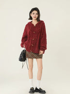 Full body shot of a woman in a burgundy cable knit hooded cardigan and plaid mini skirt.