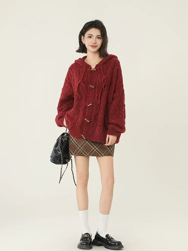 Full body shot of a woman in a burgundy cable knit hooded cardigan and plaid mini skirt.